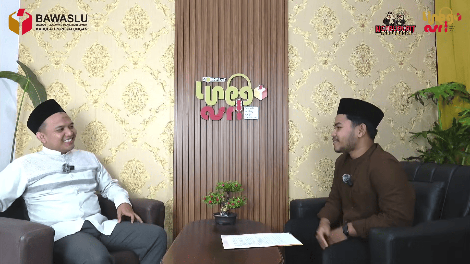 Ayon Diniyanto (narasumber) dan Sholawat Takbir Jagad Lanang (host) sedang melakukan podcast, dengan posisi narasumber di sebelah kiri dan host di sebelah kanan dari sudut pandang layar.